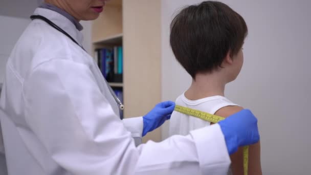 病院で白人少年の肩と頭を測定する認識できない医師 小児科専門医が診療所内で小児の身体を屋内で測定 — ストック動画
