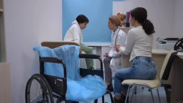 Close Wheelchair Hospital Blurred Caucasian Son Mother Consulting Doctor Background — Stock Video