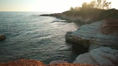Günbatımında Kıbrıs Rum Kesimi 'nin geniş açılı sahili, Akdeniz dalgaları yavaş çekimde dalgalanırken. Yazlık tatil beldesinde gün batımında açık havada resim gibi doğa