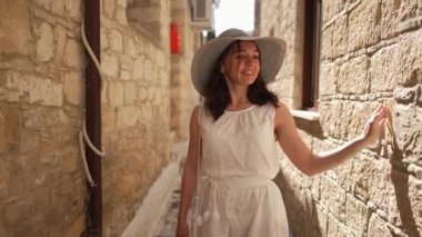 Eski şehrin güneşli dar caddesinde ağır çekimde yürüyen gülümseyen mutlu kadının portresi. Kıbrıs 'ın eski mimarisine hayran olan Kafkas turistleri etrafa bakınıyor. Gezmeye.