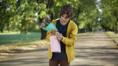 Kendine güveni tam genç bir çocuk. Hediye çantası ve bir buket çiçekle yaz parkında duruyor. Kafkasyalı ergen erkek arkadaşın portresi. Dışarıda bir randevu bekliyor. Başka tarafa bakıyor.