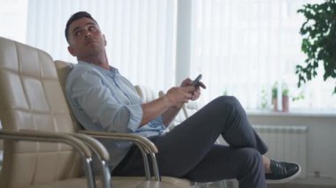 Konferans odasında rahat koltukta oturan zarif beyaz bir adam partnerini bekliyor. Ofisteki başarılı iş adamı akıllı telefondan internette sörf yapıyor.