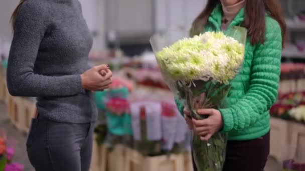 侧视看不见的女人穿过一束美丽的花朵站在室内 满意的买方和专业卖方在花店谈论购买植物 — 图库视频影像