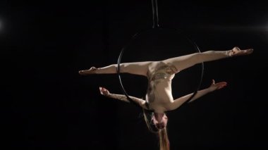 Geniş açılı, zayıf, genç bir kadın siyah arka planda asılı duran hava çemberinde numaralar yapıyor. Esnek yetenekli Kafkas hava akrobatı performans eğitimi