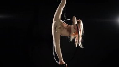 Geniş açılı hava jimnastikçisi, uzun saçları sallayarak dönen hava çemberinde ikiye bölündü. Siyah arka planda akrobasi yapan profesyonel ince beyaz kadın portresi. Sanat ve spor konsepti