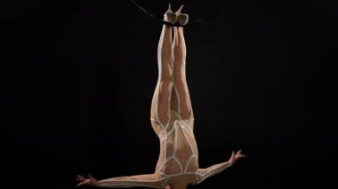 Sıska, güzel, kızıl saçlı, ayakları havada asılı bir kadın. Yetenekli, baştan çıkarıcı, beyaz tenli, gülümseyen bir jimnastikçinin geniş açılı portresi.