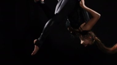 Zayıf, çıplak ayaklı, hava çemberini deviren siyah arka planda numaralar yapan genç bir kadınla yürüyen. Sahnede kendine güvenen beyaz hava jimnastikçisi performans sergiliyor.