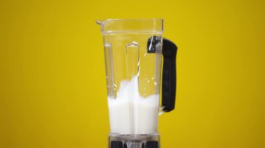 Sarı arka planda sütle yakın çekim mikseri ve kırmızı çilekler yavaş çekimde sıvıya dökülüyor. Sağlıklı vitamin kokteyli hazırlığı. Sağlıklı yeme kavramı