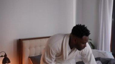 Mutlu Afrikalı Amerikalı genç adam yatağa gülümseyerek giriyor. Tatmin olmuş yakışıklı adamın portresi evde uyuyakalıyor. Günlük rutin ve mutluluk kavramı