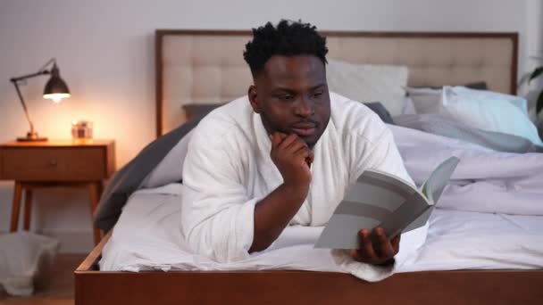 Поглощённый Афроамериканец Читающий Книгу Лежащую Дома Кровати Портрет Умного Уверенного — стоковое видео