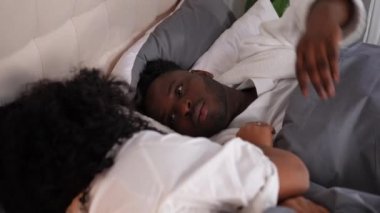 Mutlu genç adamın portresi yatakta uzanmış konuşan kadına sarılıyor. Yakışıklı Afrikalı Amerikalı erkek arkadaş evde dinlenen güzel kız arkadaşa sarılıyor.