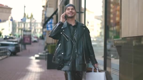自信を持って電話を残して話を買い物袋で歩くゲイの男を満足させた 市内中心部で買い物をしながらスマートフォンでおしゃべりする陽気な白人Lgbtqの人物の肖像 — ストック動画