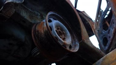 Otomobil çöplüğünde lastiği olmayan yakın çekimde yanmış bir araba tekerleği. Ukrayna 'da savaş bölgesinde tahrip edilmiş bir araç. Rus işgali ve askeri gerginlik kavramı