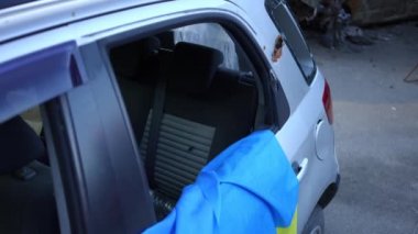 Kapısında Ukrayna bayrağı asılı ve kurşun delikleri olan terk edilmiş bir araba. Canlı kamera, Ukrayna 'daki savaş bölgesinde tahrip edilmiş otomobil boyunca geri gidiyor.