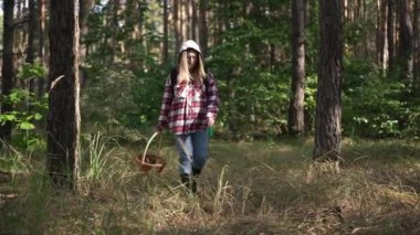 Ormanda mantar arayan kendine güvenen genç bir kadın ve önünden geçen bir ağaç. Yoğunlaştırılmış beyaz kaşif toplayıcı gün ışığında ağır çekimde geziniyor.