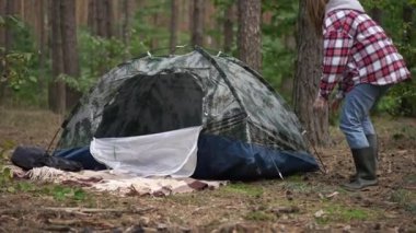 Ormanda kamp çadırını yavaş çekimde söken genç bir kadın. Ormanlık alanda sakin çayırlarda gezen kendinden emin beyaz gezginin geniş açılı portresi. Çevre turizmi ve neşesi