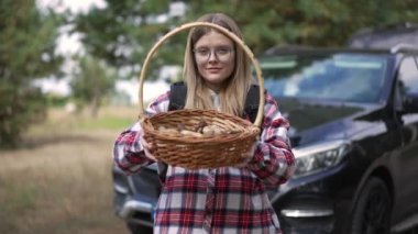 Ormanda mantarla poz veren kendine güvenen güzel bir kadının ön manzara portresi. Gülümseyen beyaz gezginden mantarlı sepete odaklan.