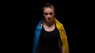 Ukrayna bayrağında karanlıkta yürüyen bir kadın yüz ifadesini umut ederek kameraya bakıyor. Siyah arka planda poz veren genç ve güzel bir bayan. Umut ve savaş kavramı