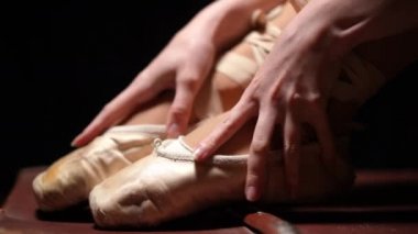 Kadın elleri siyah arka planda bej noktalarda ayaklarını okşuyor. Tanınmayacak kadar yetenekli zarif balerin, bale ayakkabılarıyla bacakları okşuyor.