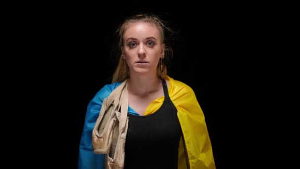 穿着乌克兰国旗 肩膀上挂着尖头的可悲的年轻女子看着镜头 灰心丧气的女子面容绝望地在黑色背景下的画像 — 图库视频影像