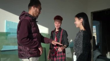 Multiethnic friends failing handstack in slow motion laughing. African American man, Asian and Caucasian women having fun standing in sunshine in building under construction