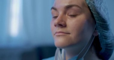 Headshot of young confident woman in medical uniform taking off Covid face mask drinking tea in slow motion smiling. Satisfied beautiful Caucasian doctor enjoying drink in hospital. Cinema 4k ProResHQ