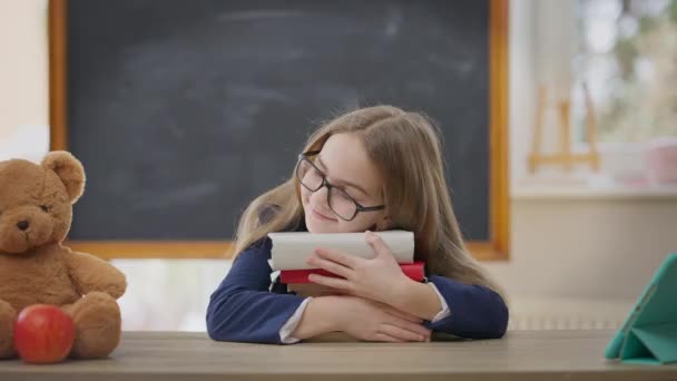 Smiling Schoolgirl Eyeglasses Hugging Books Sitting Desk Classroom Looking Camera – stockvideo