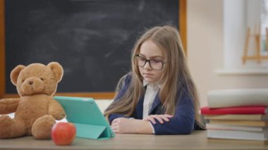 Ciddi odaklanmış liseli kız el sıkışmadan el sıkışarak tabletle evde oturuyor. Online sınıfta okuyan, kendinden emin, memnun olmayan beyaz kız portresi.