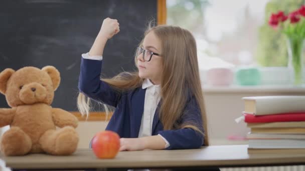 Positive Cute Schoolgirl Gesturing Strength Gesture Smiling Sitting Desk Teddy — ストック動画