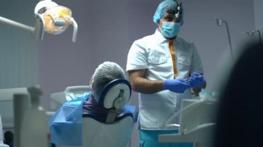 Rack focus from confident Middle Eastern dentist preparing anesthesia injection to assistant passing in slow motion with medical tools. Professional doctor and nurse preparing treatment in hospital