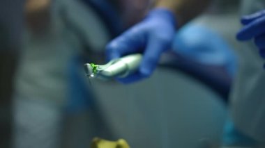 Erkek elinin içine su püskürten tek kullanımlık eldivenlerle yakın plan diş matkabı. Tanımlanamayan genç Orta Doğulu dişçi diş macununu kapalı bir klinikte kontrol ediyor. Yavaş çekim