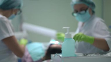 Disinfectant in dental office with blurred doctor and assistant curing patient at background. Caucasian professional women in face mask treating client in medical clinic. Insurance and medicine