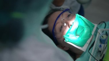 Kafkasyalı bir kadının dişçi sandalyesindeki kauçuk barajdaki yüksek açılı portresi. Doktor diş kanalına kök kanal dosyası yerleştiriyor. Tanımlanamayan diş hekimi, hastanedeki hastalar için iç mekanda işlem yapıyor.