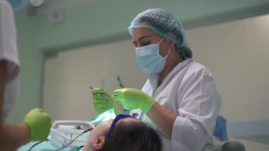 Medium shot of professional dentist in face mask curing patient in slow motion with assistant passing at front. Confident Caucasian doctor and nurse in hospital with woman in dental chair