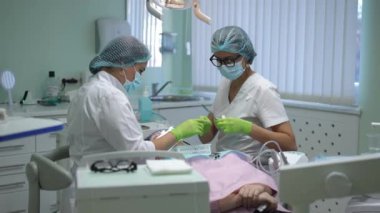 Expert Caucasian dental assistant passing sterile instrument to dentist in slow motion in hospital. Patient in dental chair undergoing treatment as concentrated women curing ill tooth. Stomatology