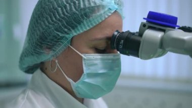 Diş mikroskobunda odaklanmış profesyonel ortodontistin yavaş çekimde ışıldayan görüntüsü. Kafkas dişçisine yakın plan, hastanedeki hastayı kapalı alanda tedavi ediyor.