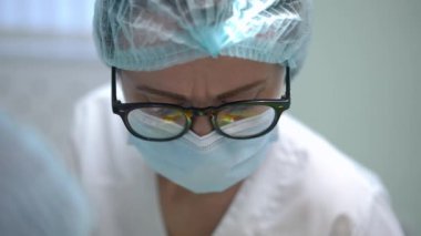 Headshot portrait of concentrated dentist in eyeglasses and face mask curing patient in hospital. Focused Caucasian woman turning treating ill tooth in slow motion. Stomatology and medicine