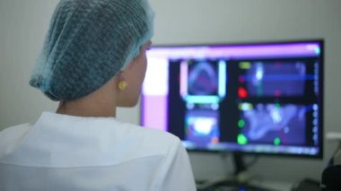 Arka planda konsantre ortodontist çene ve dişlerin 3 boyutlu görüntüsünü bilgisayar monitöründe inceliyor. Kafkas dişçisinin omzunun üstünden ağır çekimde diş röntgenini analiz ediyor.