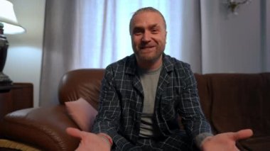 İnternette, olumlu adamın selamlaşarak kameraya baktığını gösteren bir sohbet videosu. Oturma odasındaki kanepede oturmuş pijamalı, internetten mesajlaşan, kendinden emin, Kafkasyalı, serbest bir beyazın portresi.