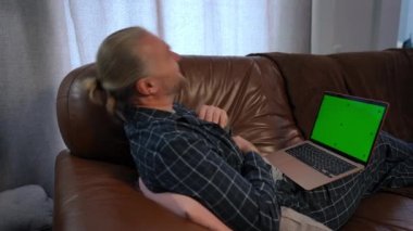 Yeşil ekranda online film izlerken gülen neşeli bir adam. Pijama giymiş, hafta sonları evde boş vakit geçiren kaygısız beyaz adamın yan görünüm portresi. Model şablonu