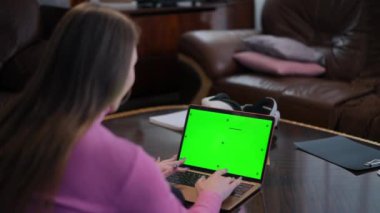 Green screen laptop with unrecognizable Caucasian young woman typing on keyboard. Slim female freelancer messaging online on chromakey device sitting in home office indoors. Remote working concept