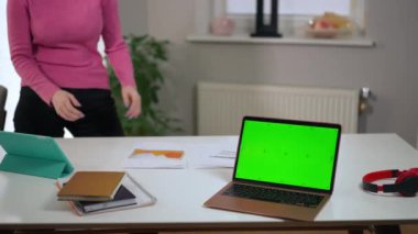 Unrecognizable troubled woman walking side to side in home office with green screen laptop on table. Worried anxious startuper freelancer thinking planning e-business indoors. Intelligence concept