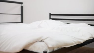 Comfortable bed in hotel bedroom with white soft pillows falling in slow motion. Wide shot cozy furniture in room indoors. Leisure and relaxation concept