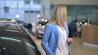 Araba galerisinde yeni otomobil seçen muhteşem başarılı iş kadını. Düşünceli beyaz kadın portresi etrafa bakınıyor ve araba almaya karar veriyor. Otomobil endüstrisi
