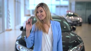 Kameraya bakıp gülümseyen, araba anahtarını işaret eden mutlu beyaz kadının portresi. Kendine güveni tam çekici bir alıcı araba galerisinde poz veriyor. Tüketim