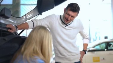 Araba galerisinde kadın ve kızla konuşan mutlu bir adamın portresi. Gülümseyen Kafkasyalı koca babası galeride ailesiyle birlikte yeni bir araba seçiyor.