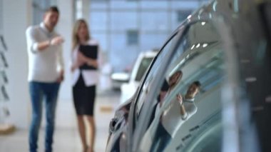 Arka planda bulanık kadın ve erkeğin konuştuğu parlak, lüks araba yan camları. Beyaz alıcılar araba galerisindeki profesyonel araba satıcılarına danışmanlık yapıyor. Yaşam tarzı ve tüketim