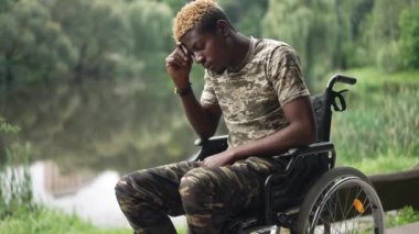 Side view devastated African American man in wheelchair thinking sitting in park on lake shore. Sad depressed frustrated soldier resting outdoors on summer day. Procrastination and disability concept
