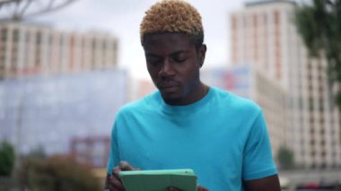 Odaklanmış akıllı Afro-Amerikalı genç adamın portresi yavaş çekim düşünen tablet dokunmatik ekranı. Yoğunlaştırılmış meşgul milenyum adamı şehir caddesinde duruyor ve başlangıç planı yapıyor.