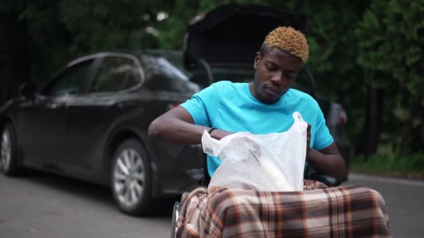Młody Afroamerykanin Wózku Inwalidzkim Zakupami Zewnątrz Zamazanym Czarnym Samochodem Tle — Wideo stockowe